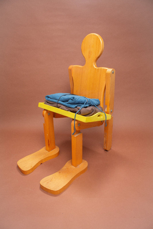 Wooden mannequin chair with blue and brown folded sweatshirts on its lap.