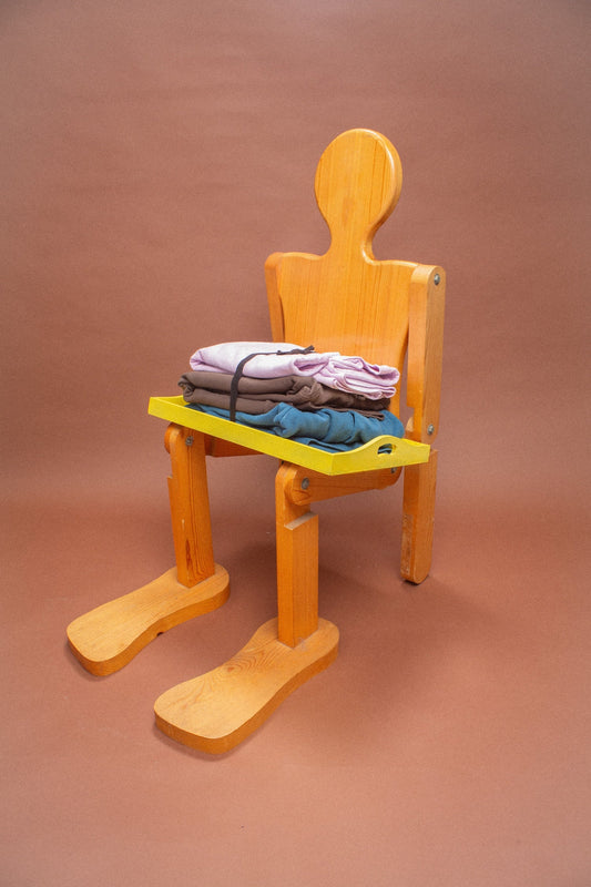 Wooden mannequin chair with Lavender and Soil sweatshirts folded on its lap.