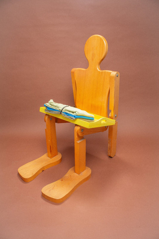 Wooden mannequin chair with Azul blue and Cardamom light green tees folded on its lap.