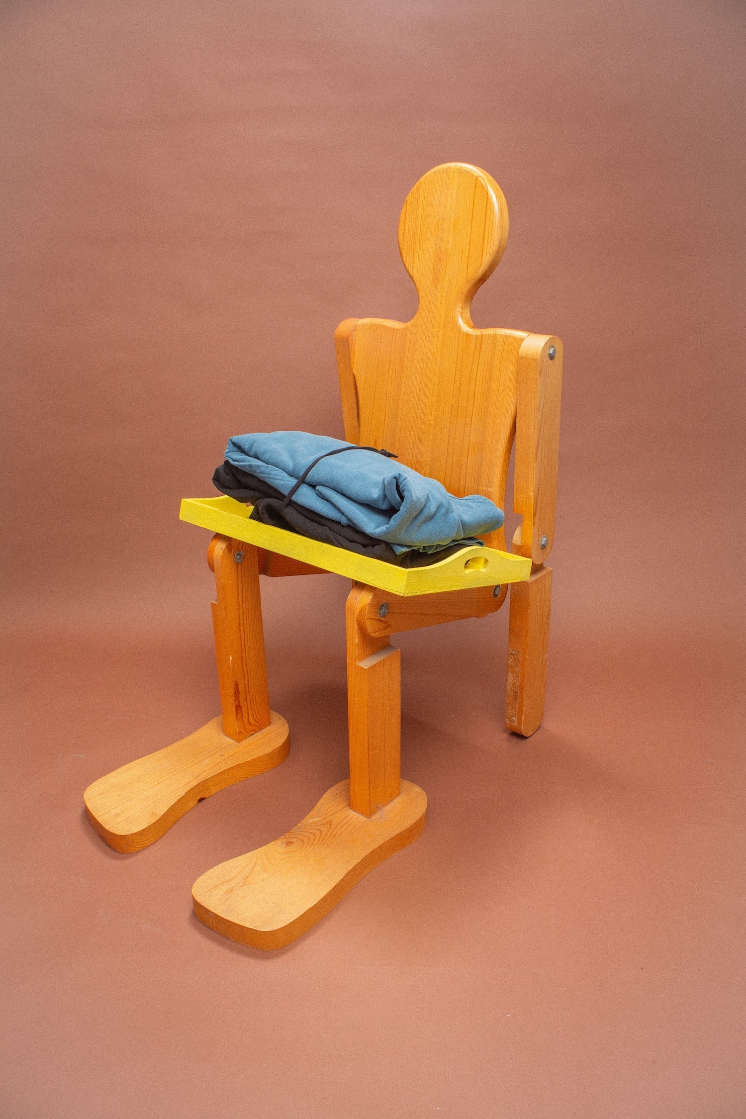 Wooden mannequin chair with blue and black hoodies folded on its lap.