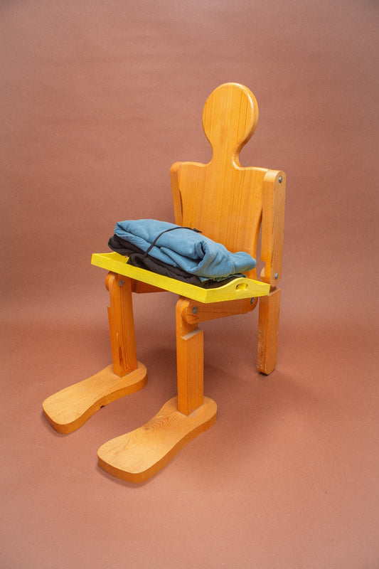 Wooden mannequin chair with blue and black hoodies folded on its lap.