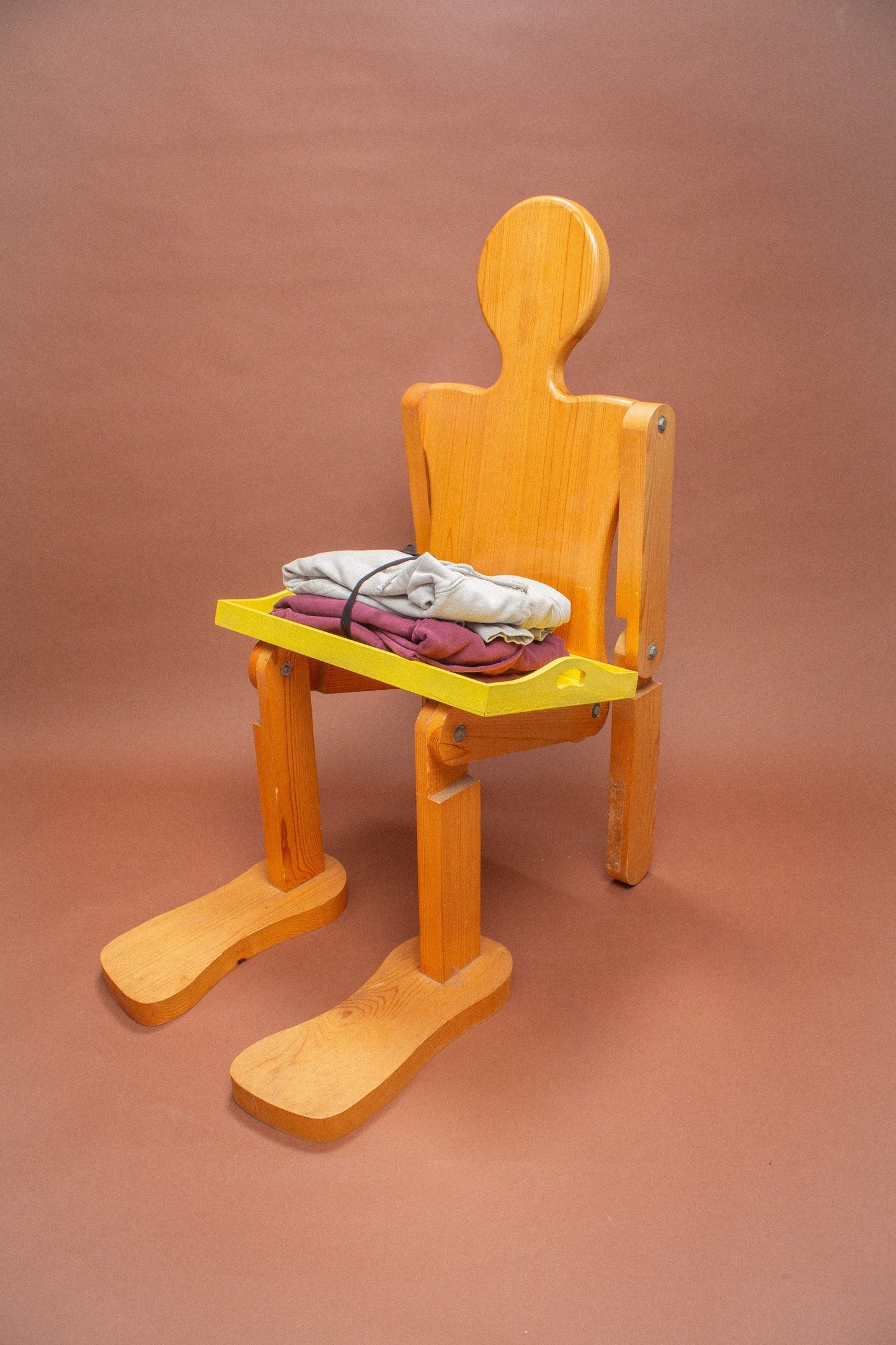 Wooden mannequin chair with Grey and Burgundy sweatshirts folded on its lap.
