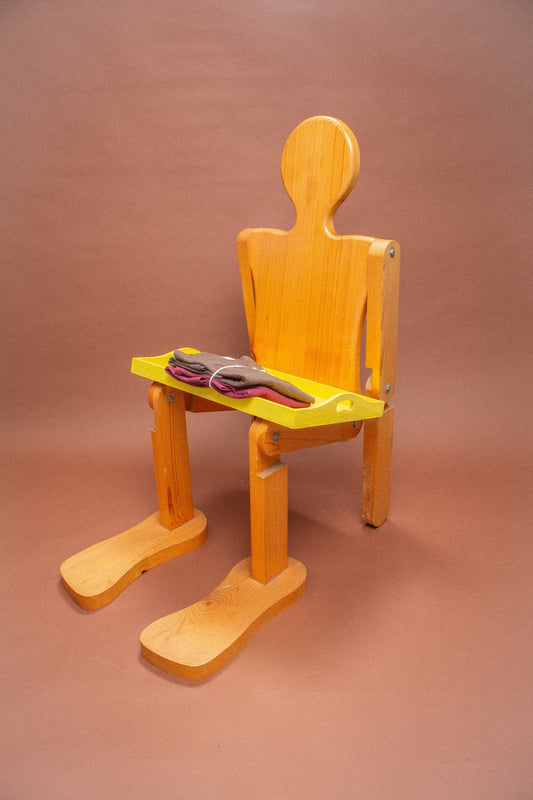 Wooden mannequin chair with Burgundy and Soil tees folded on its lap.