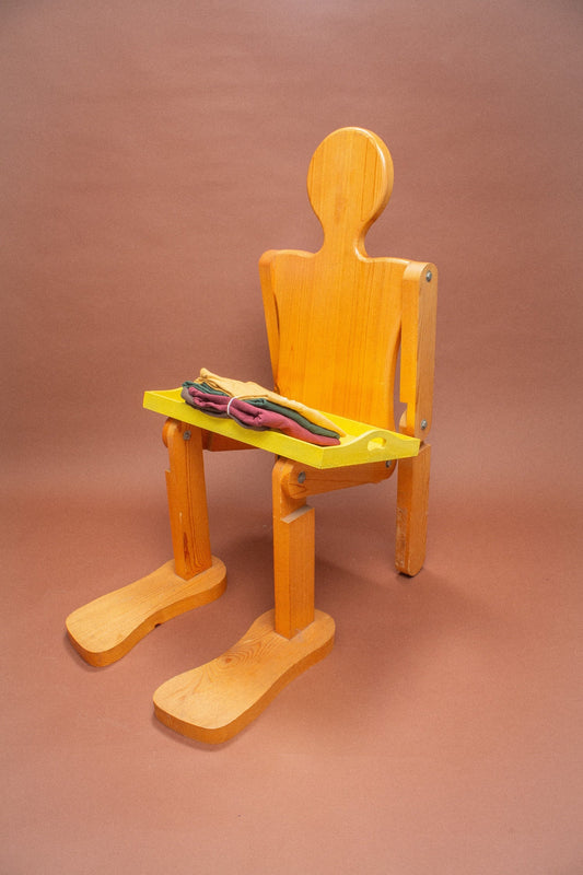 Wooden mannequin chair with Amber, Soil and Moss green folded tees on its lap.