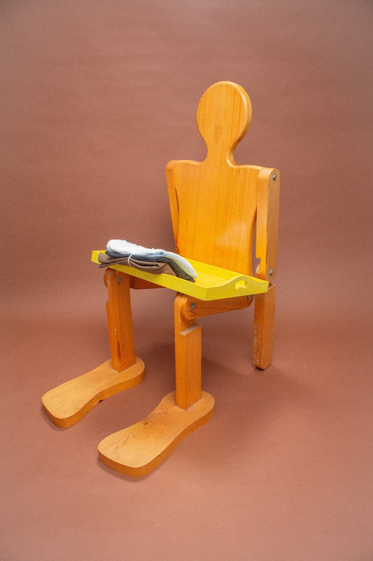 Wooden mannequin chair with White, Slate and Fog (light blue) folded tees on its lap.