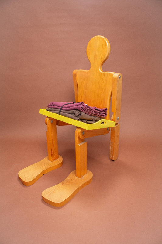 Wooden mannequin chair with Burgundy and Soil sweatshirts folded on its lap.