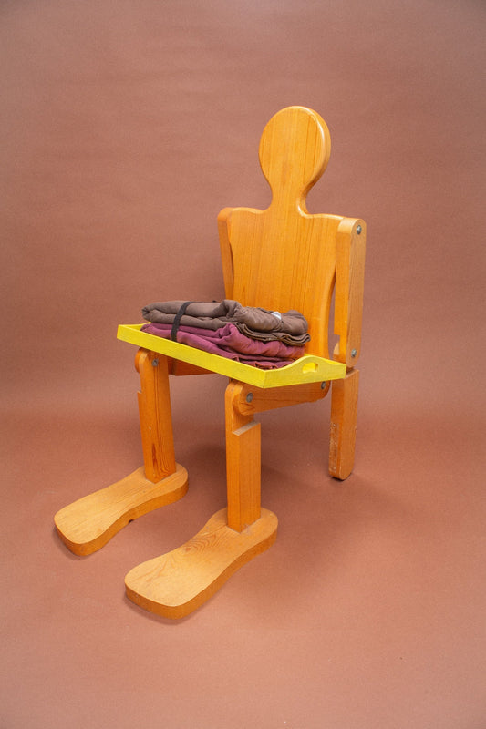 Wooden mannequin chair with Burgundy and Soil hoodies folded on its lap.