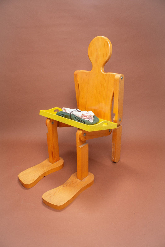 Wooden mannequin chair with folded pink shorts and green pants on its lap.