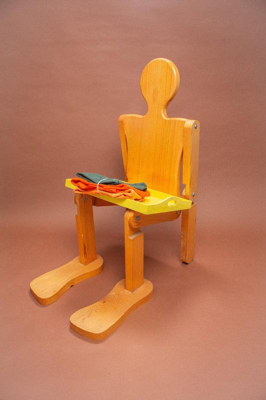 Wooden stool with peach, orange and green folded tees on it.