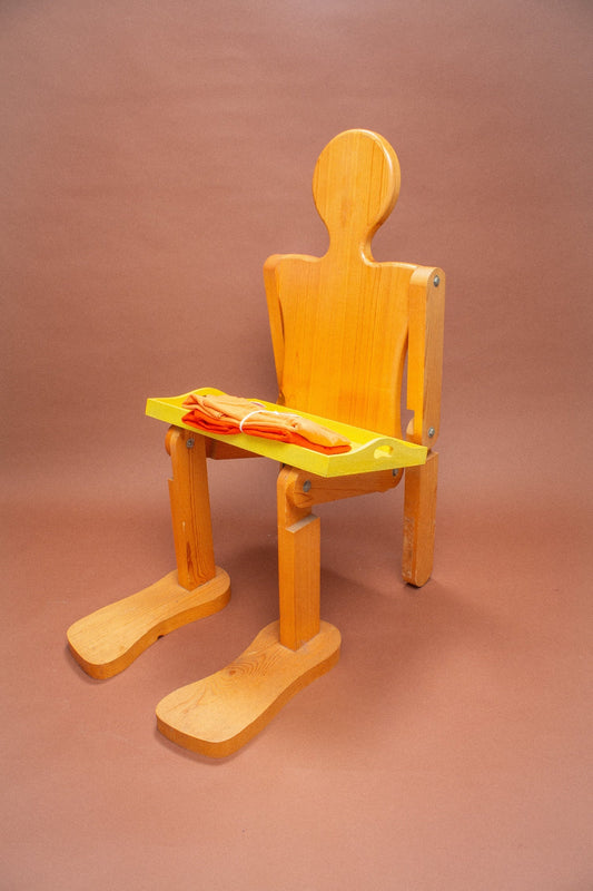 Wooden mannequin chair with peach and orange folded tees on it.