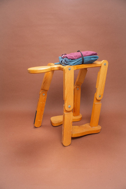 Wooden stool with blue and burgundy folded sweatshirts on it.
