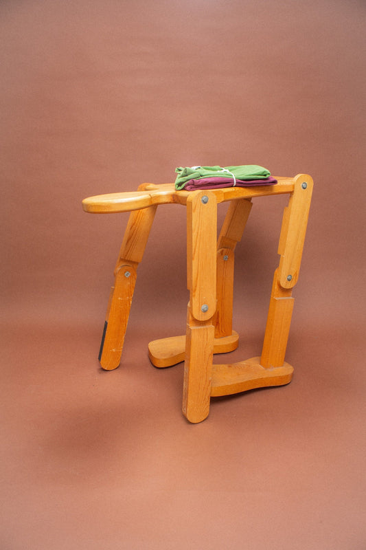 Wooden stool with folded green and burgundy tees on it.