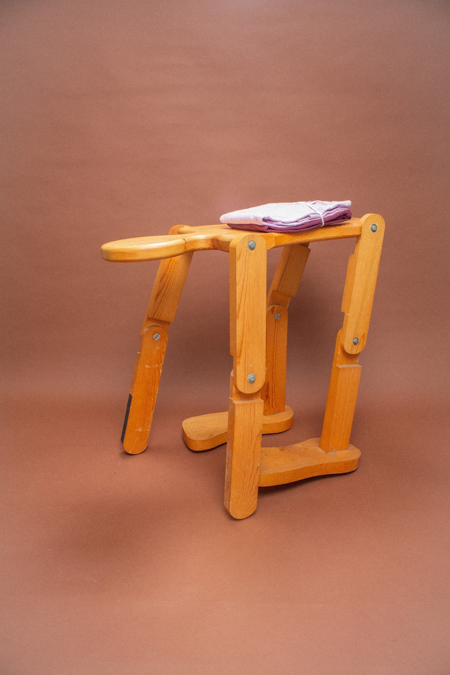 Wooden stool with folded lavender and burgundy tees on it.