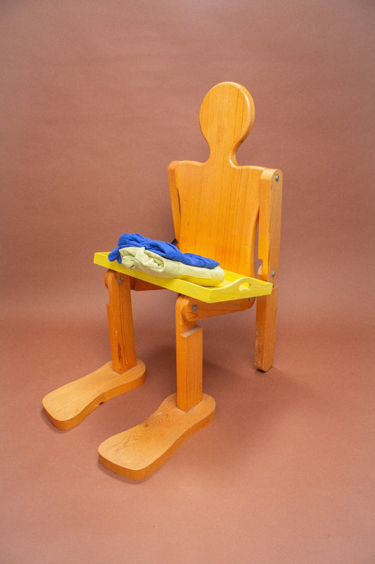 Wooden mannequin with a yellow tray holding blue and green items on a brown background