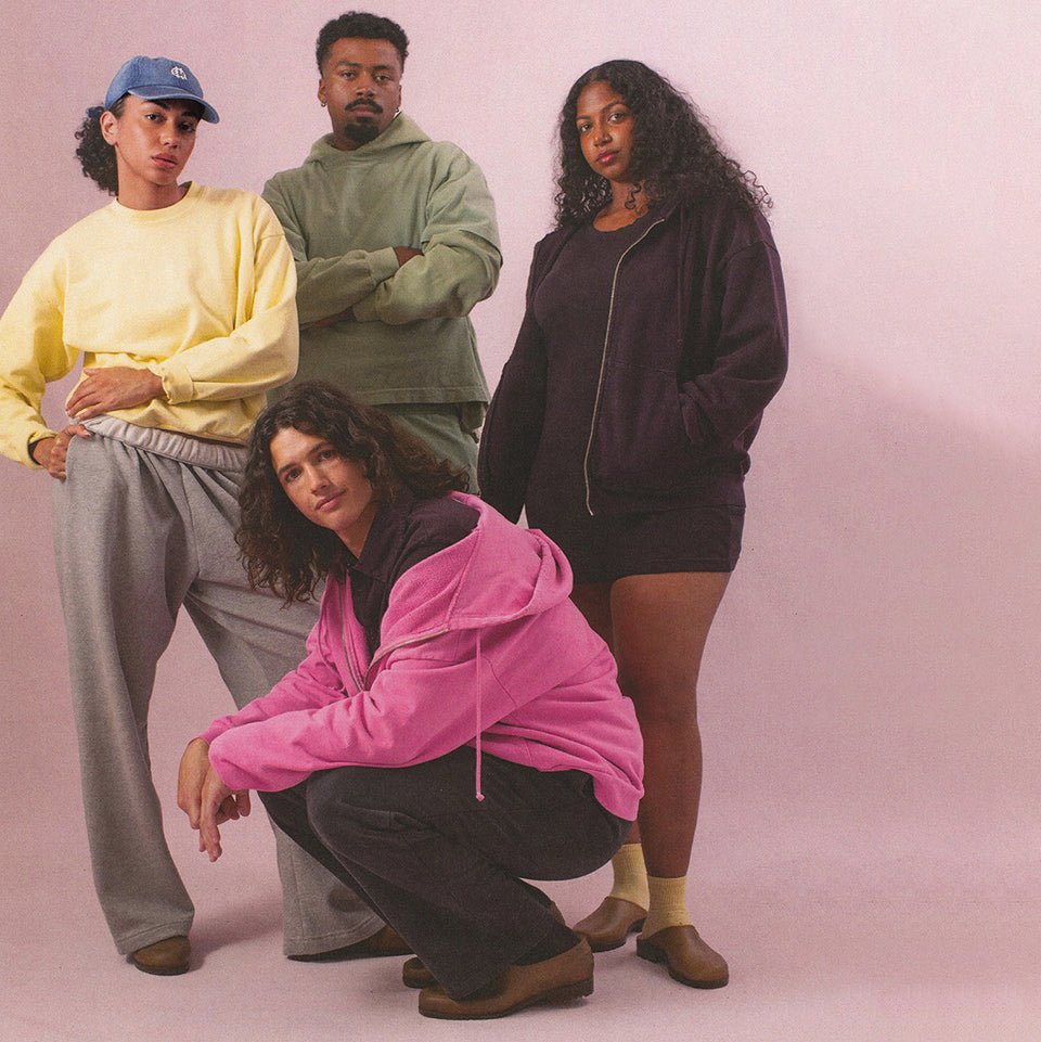 Four people posing together against a pink background, each wearing Trash Fleece in seasonal colors.