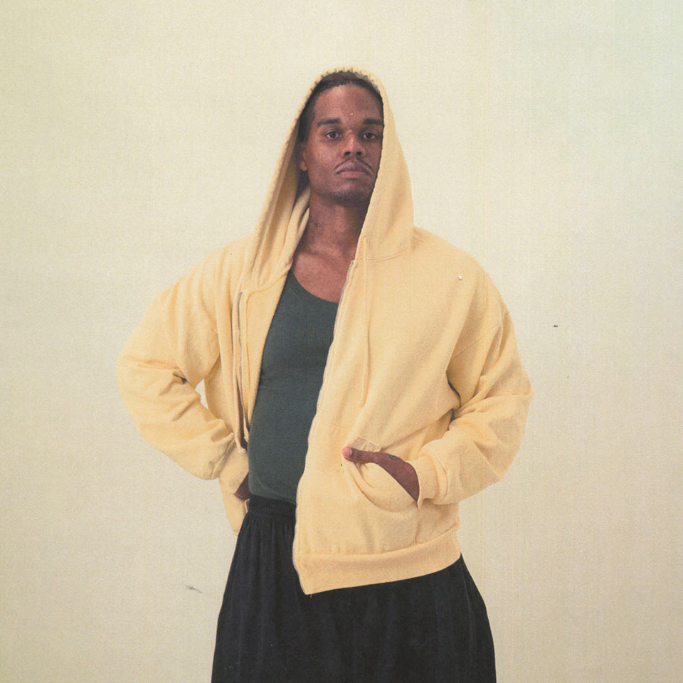 Person wearing a Trash Zip Up Hoodie in French Butter with the hood up and their hands in the pocket. 