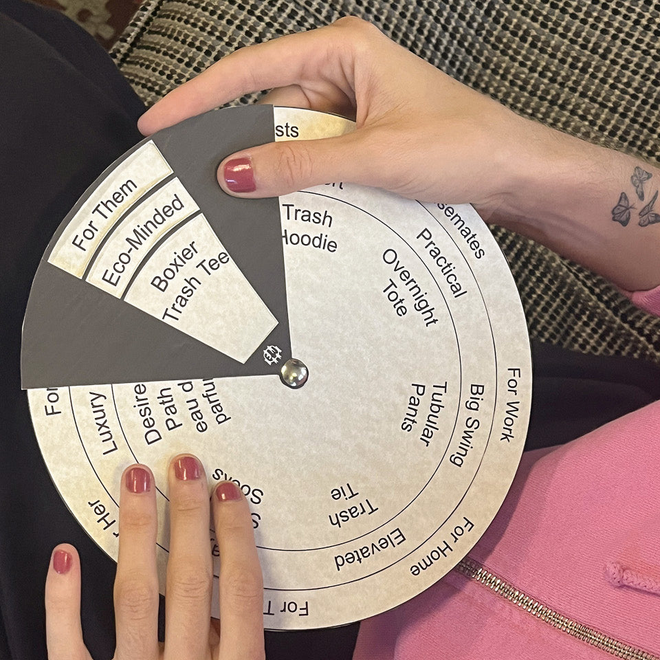 Person holding a circular selection tool with text on it, landing on "For Them, Eco-Minded, Boxier Trash Tee", wearing a Trash Zip Up Hoodie in Pixie.