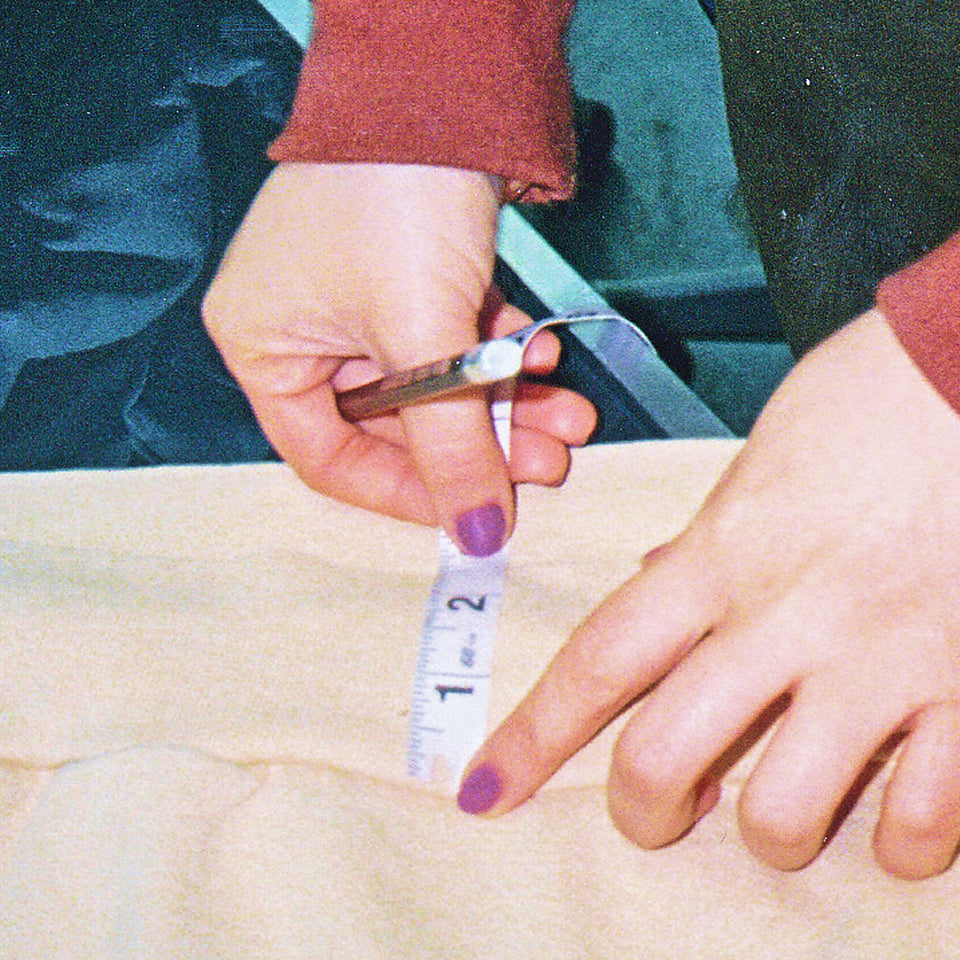 Hands holding down a measuring tape onto fabric.