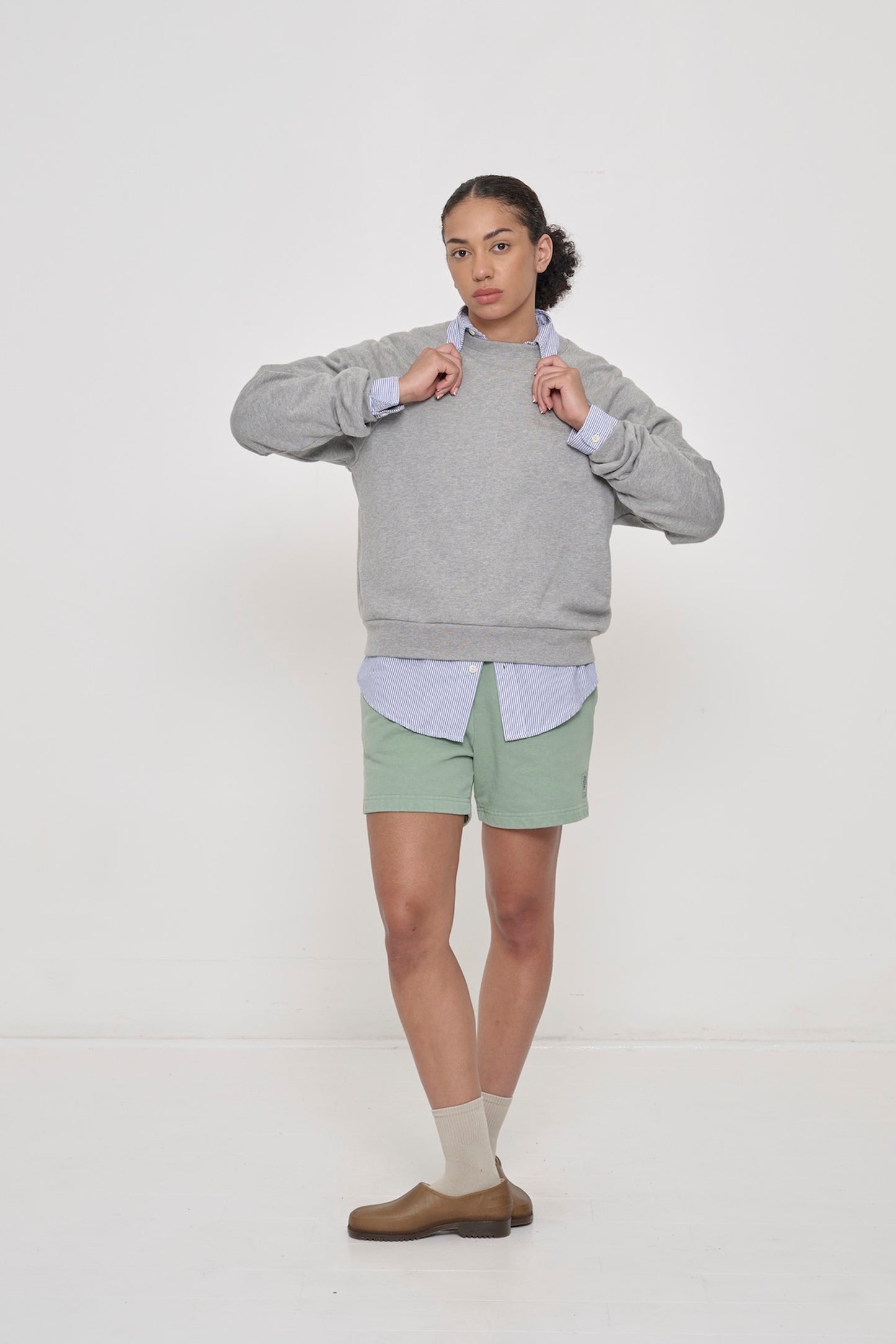 A woman in a Heather Raglan Sweatshirt worn over a Stripe Poplin Button-Up Shirt with Trash Fleece Everyday Shorts.