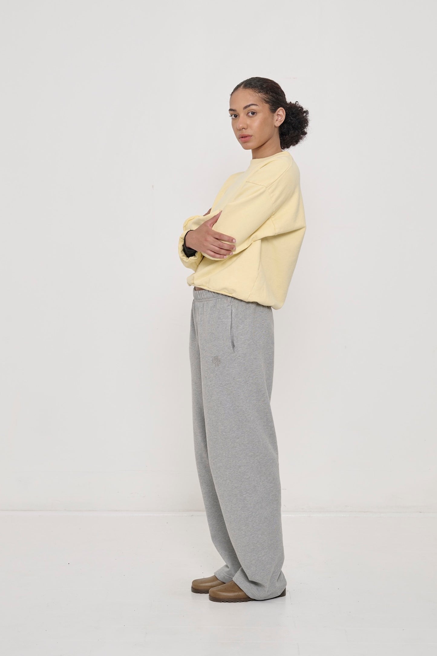 A woman in Heather Sweatpants and a French Butter Trash Crewneck with arms crossed.