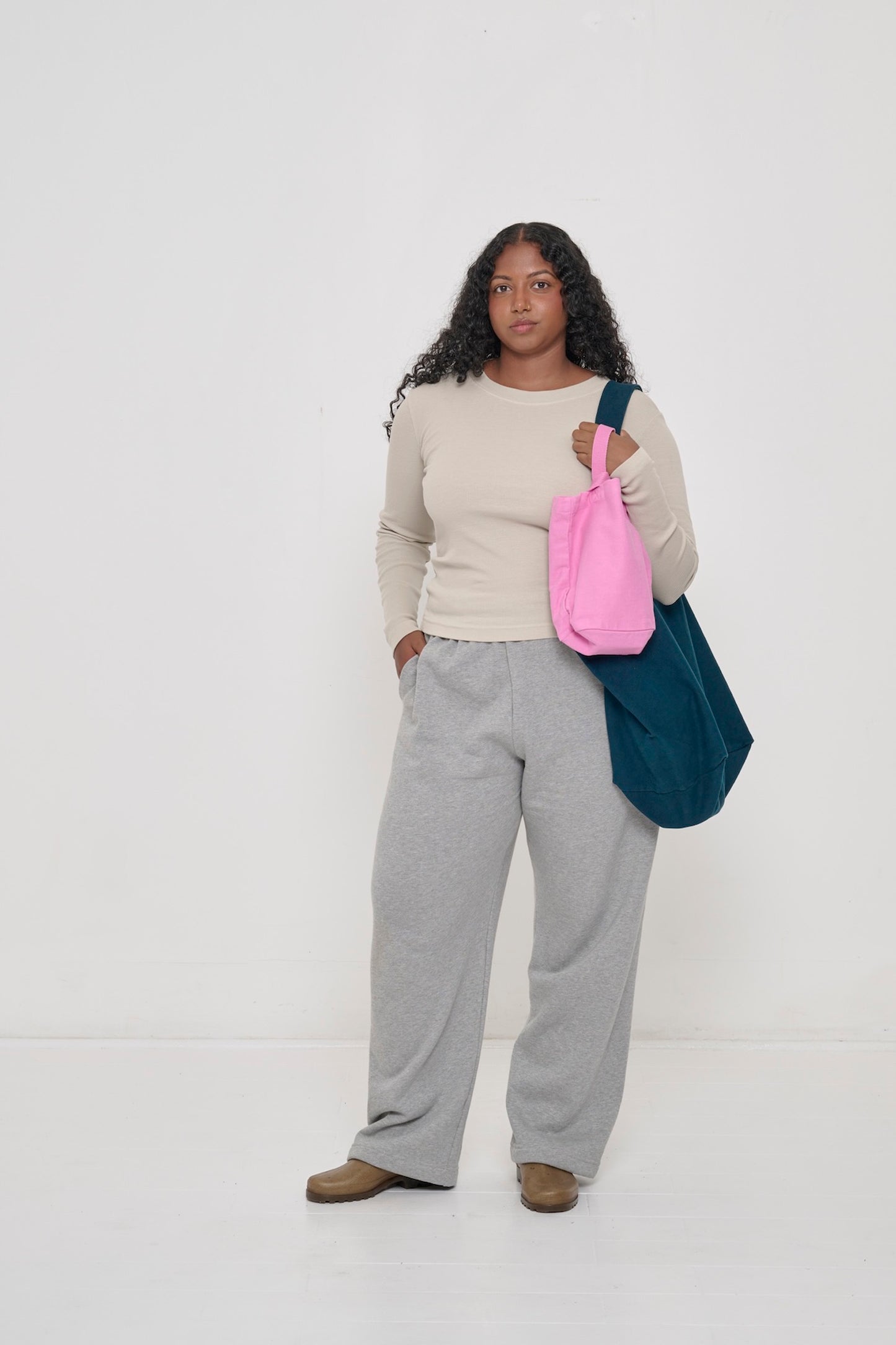 Woman in a Boxier Long Sleeve Thermal Trash Tee and Heather Sweatpants, with a Big Tote and a Loop Tote, one hand in her pocket.
