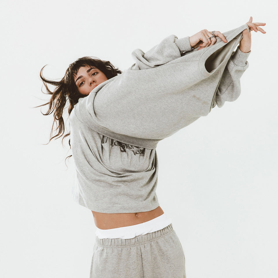 Woman pulling a Heather Raglan Sweatshirt over herself, wearing Heather Boxier Tee and Heather Sweatpants.