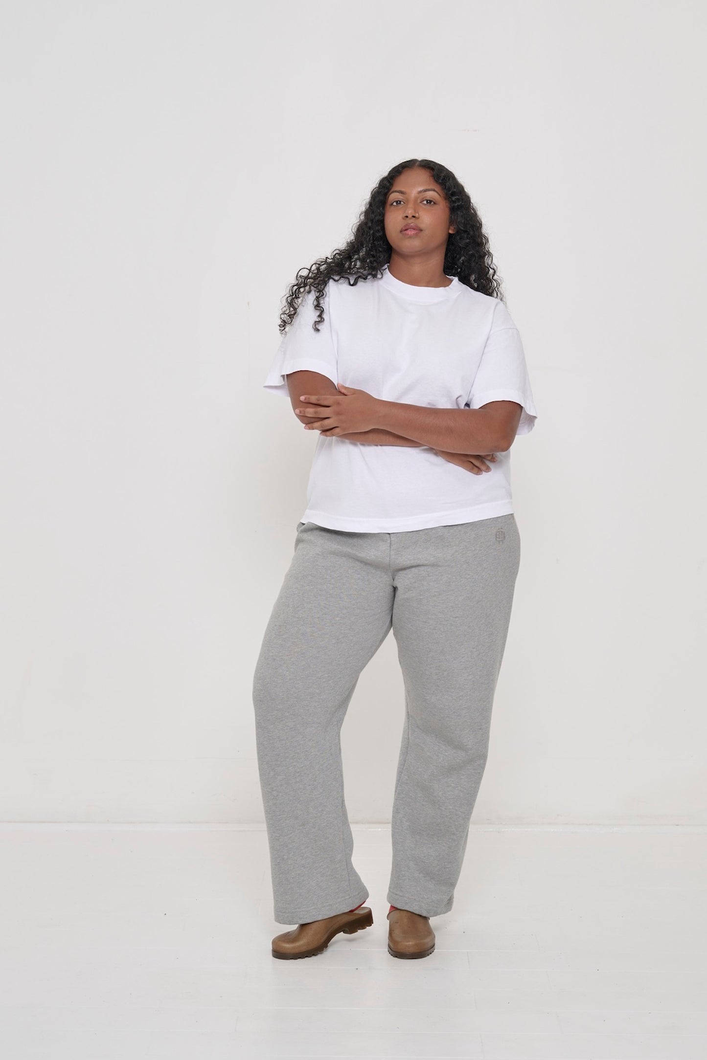 A woman in a White Heavyweight Boxier Trash Tee with Heather Sweatpants and Plasticana Opana Mules.