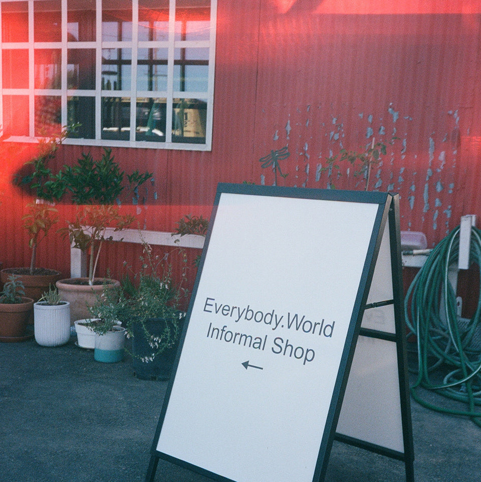 Sandwich board sign out front a red building that reads Everybody.World Informal Shop with an arrow pointing to the left.