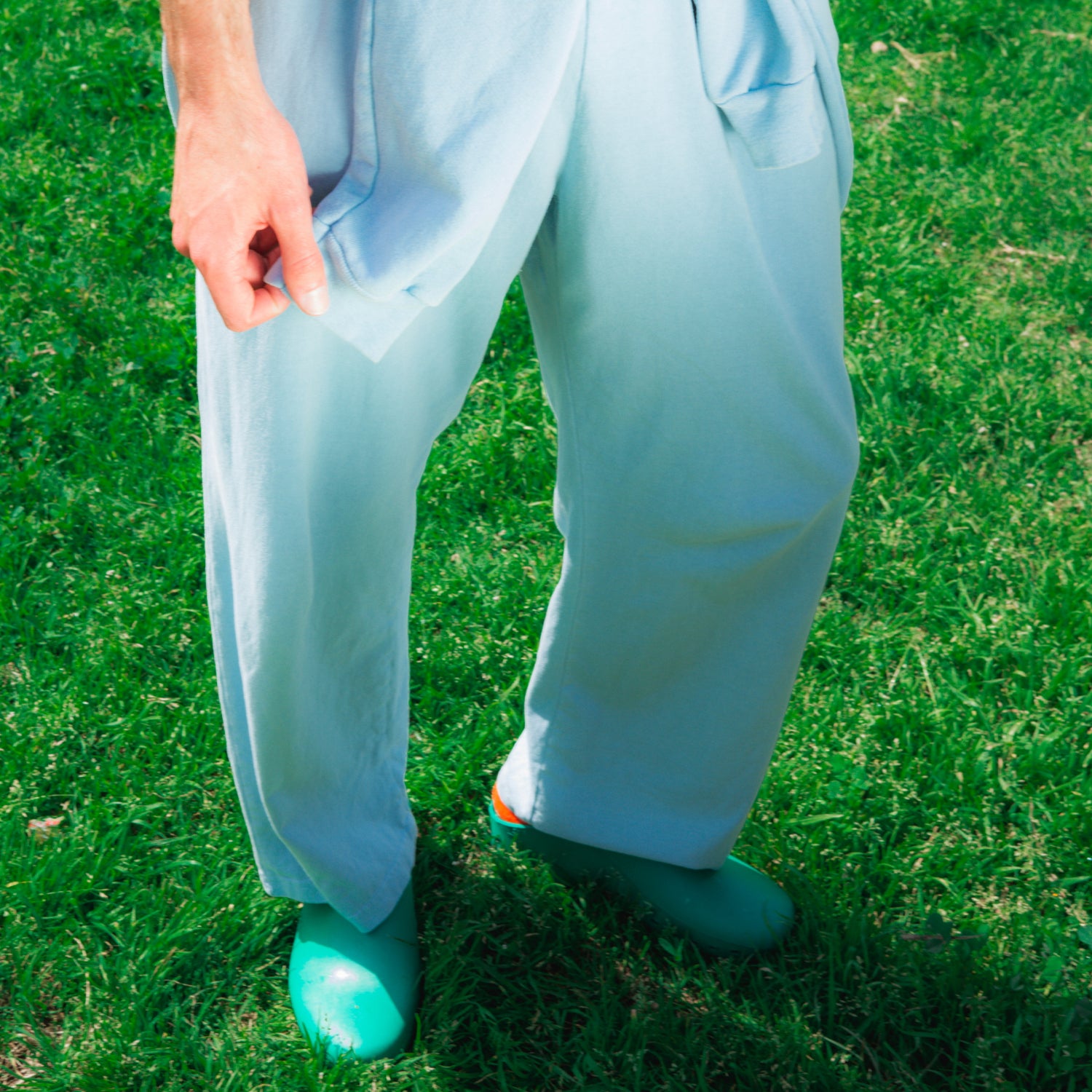 Image of a model's legs standing on lush green grass, he is wearing Apartment Pants and Calzuro Clogs