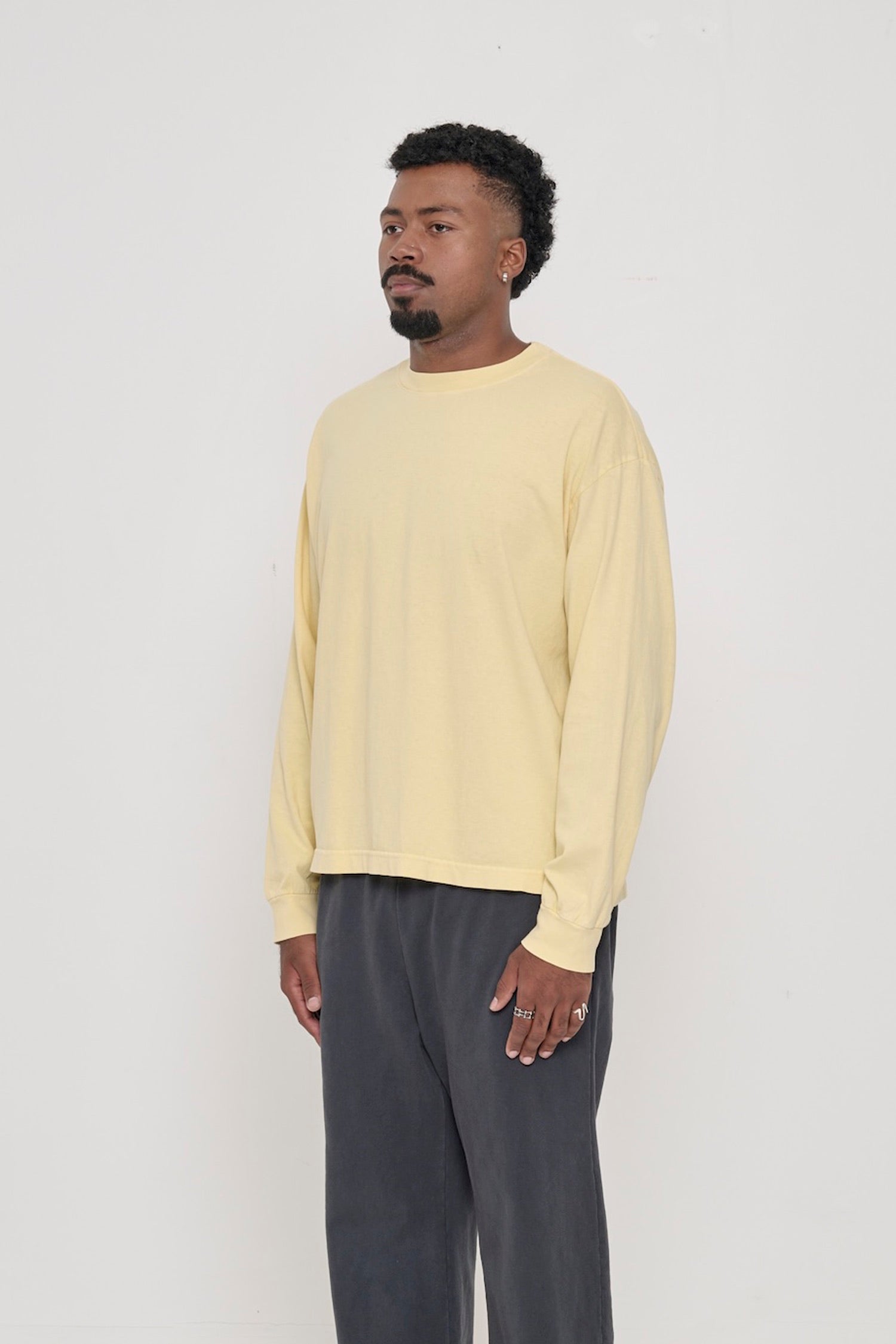 A person facing 45-degrees from the front, in a French Butter Long Sleeve Boxier Trash Tee. Relaxed sleeves and rib cuff.