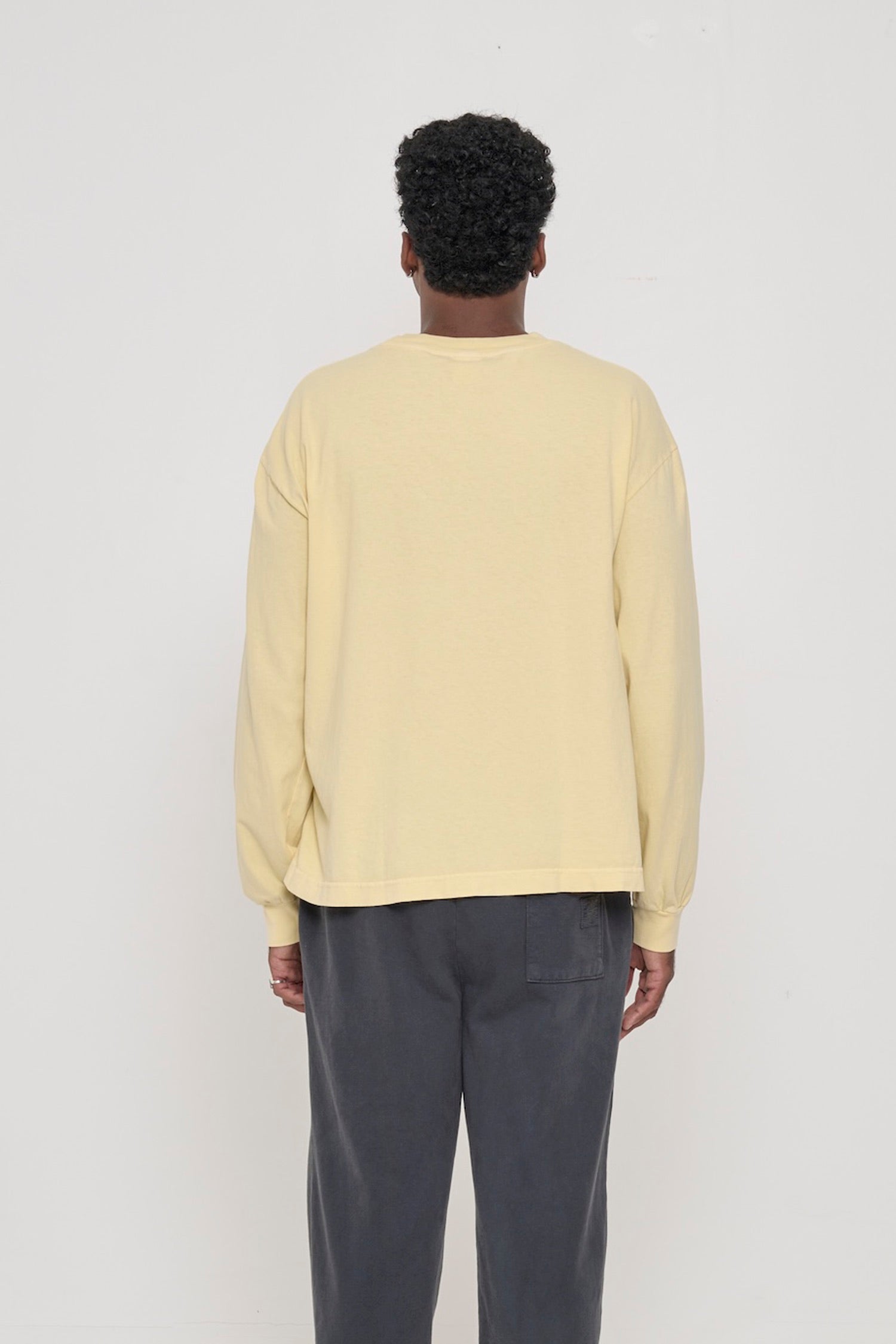 Back view of a person in a French Butter Long Sleeve Boxier Trash Tee. Relaxed fit throughout.