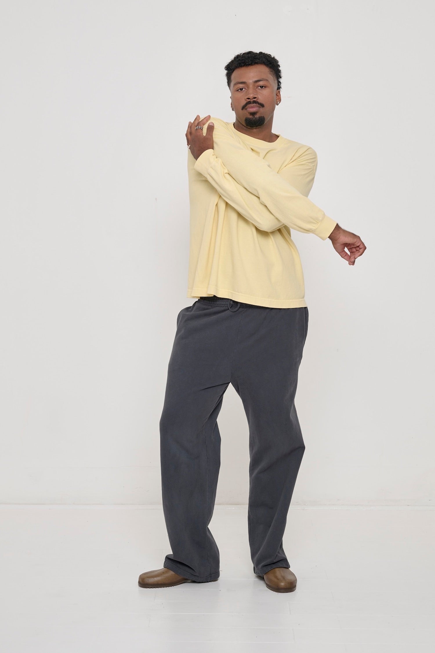 A man holding onto his opposite shoulder, wearing a French Butter Long Sleeve Boxier Trash Tee. Shows easy movement in the shirt.