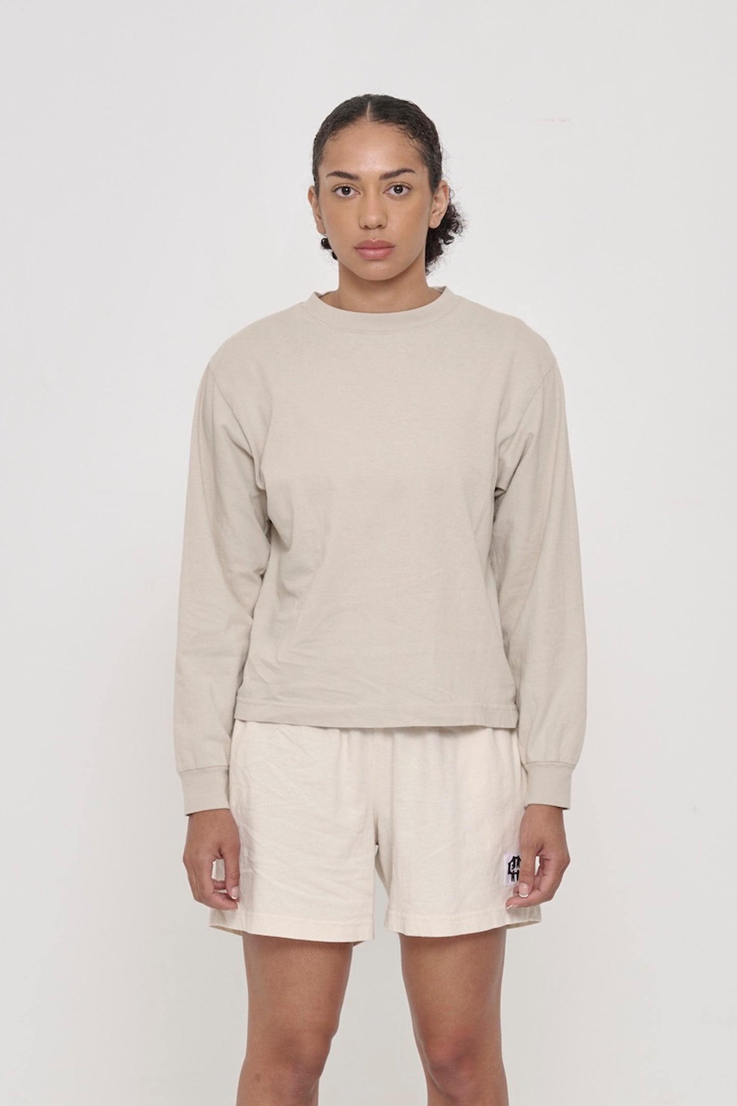 A woman in an Oat Long Sleeve Boxier Trash Tee. Shirt hem hits the middle of the hip. 