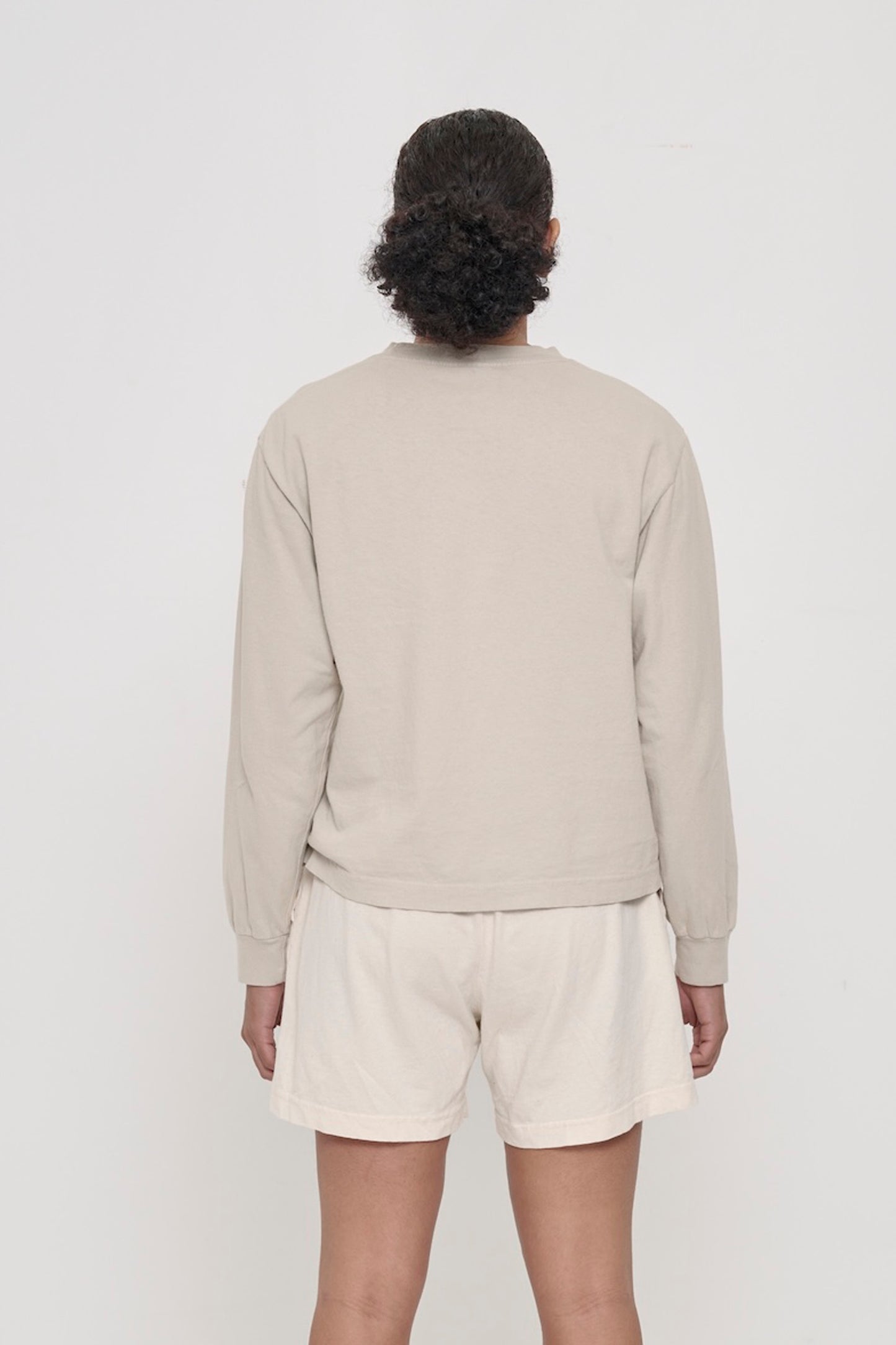 Back view of a person wearing an Oat Long Sleeve Boxier Trash Tee showing fabric drape and relaxed fit throughout.