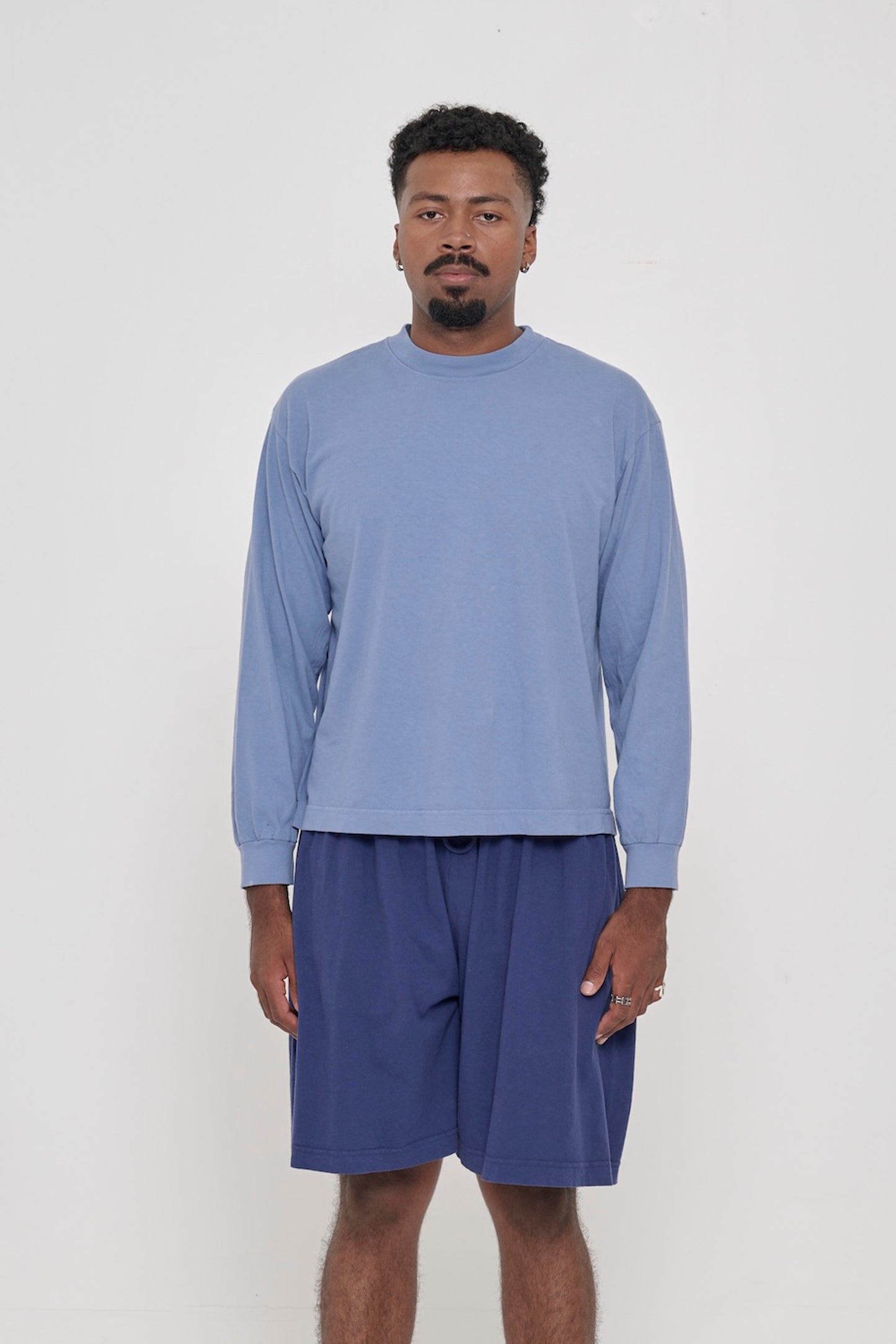 A man in a Periwinkle Long Sleeve Boxier Trash Tee. Shirt hem hits the middle of the hip. 