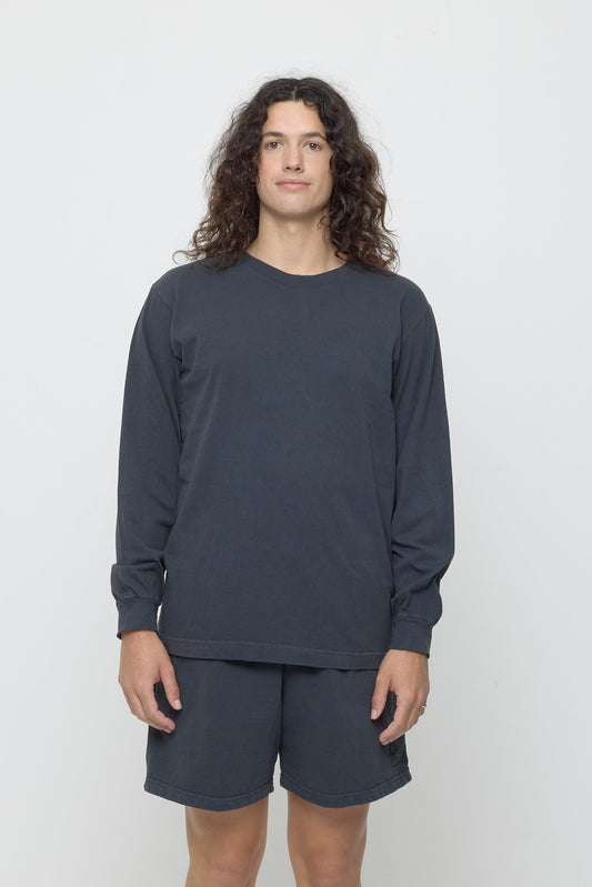 Closeup of a 6' person wearing a Slate Long Sleeve Trash Tee in size M. Their arms are straight down at their sides and shirt hem hits the lower hip. 