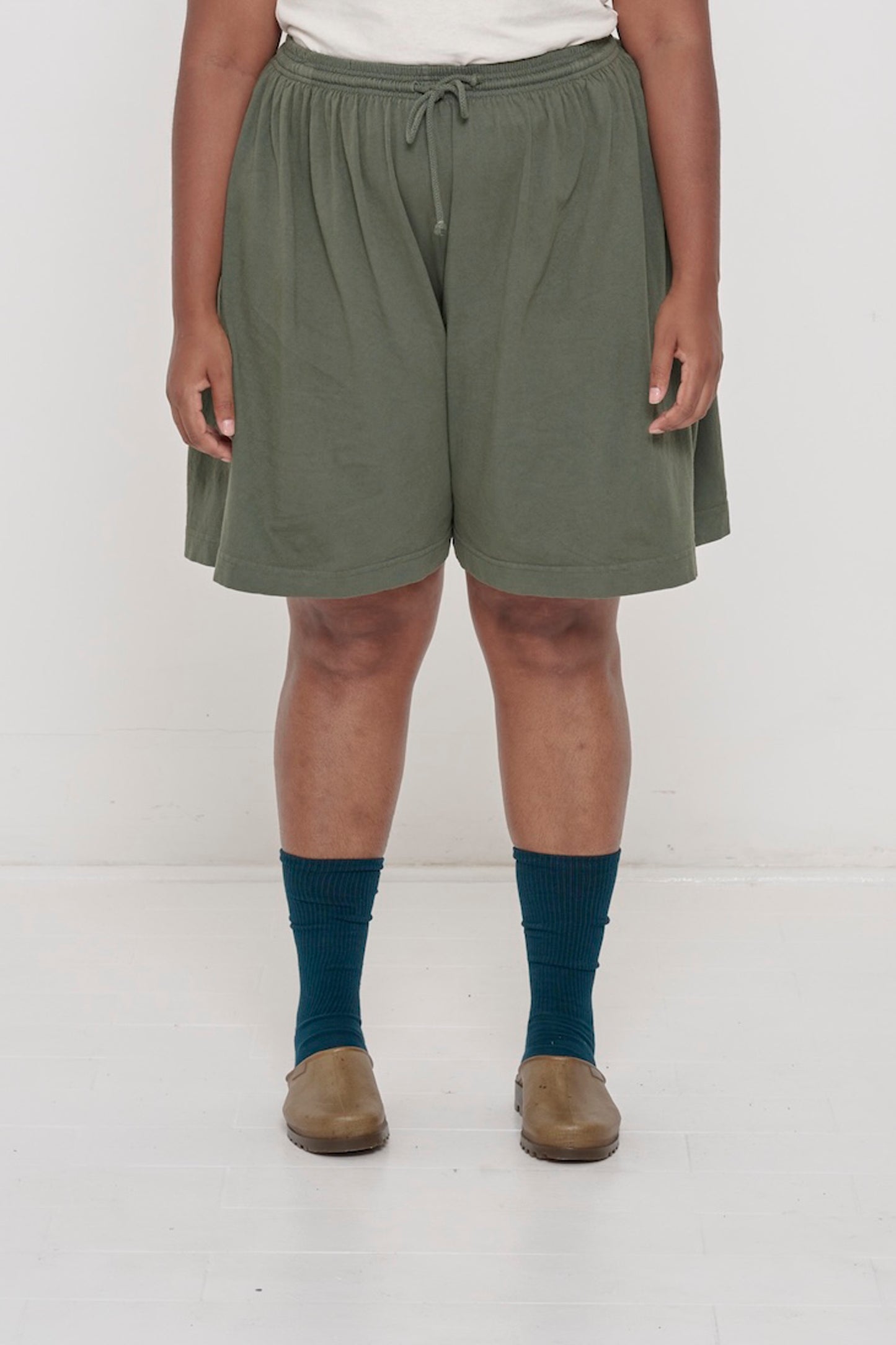 Front view woman in Pine Long Tubular Shorts, with waistband at the natural waist and  hem just above the knee.