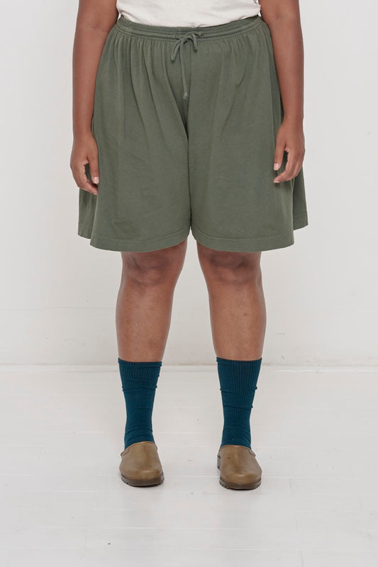Front view woman in Pine Long Tubular Shorts, with waistband at the natural waist and  hem just above the knee.