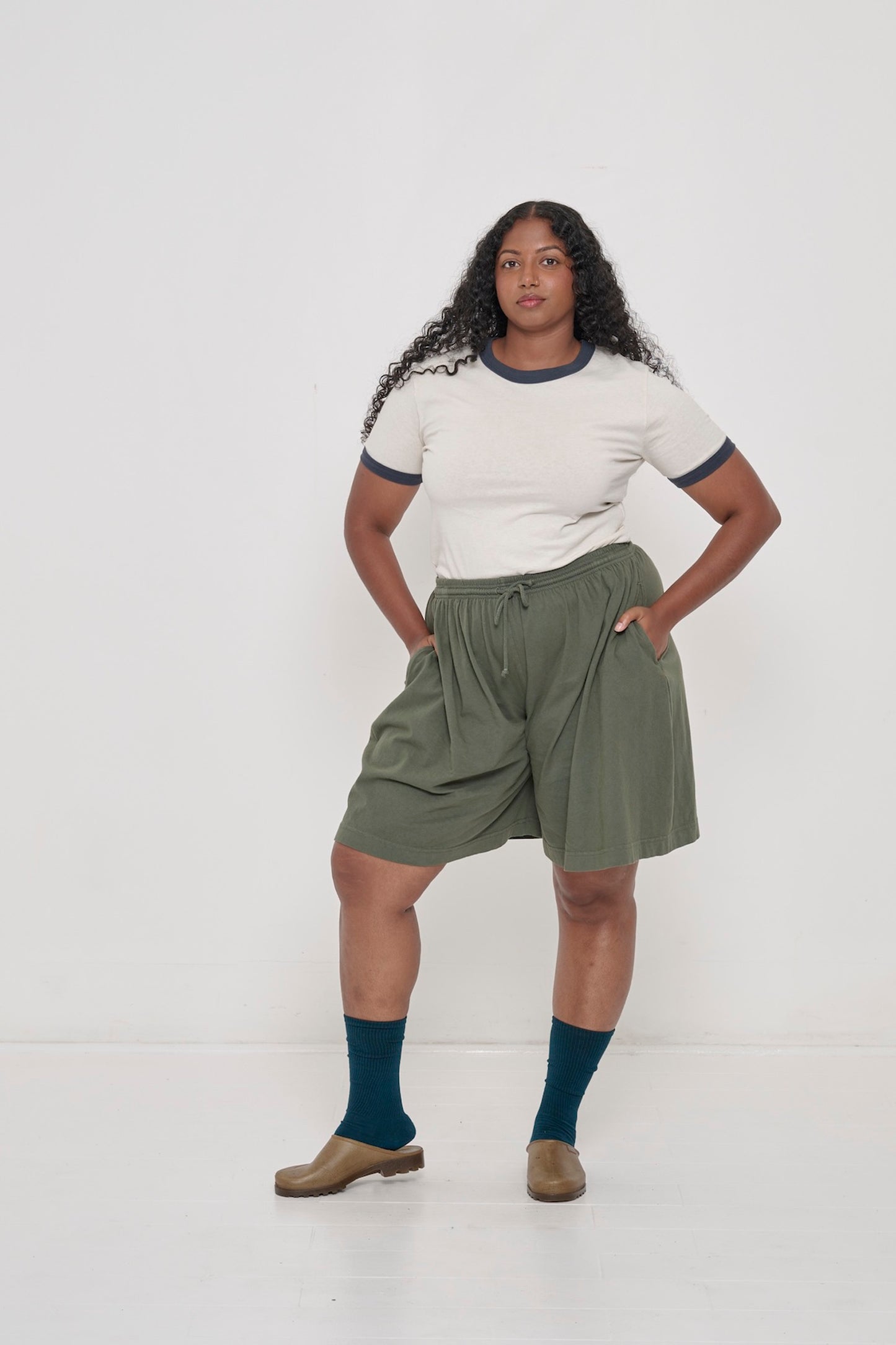 Front view of a woman in Pine Long Tubular Shorts with the Ringer Trash Tee in Slate tucked in. 
