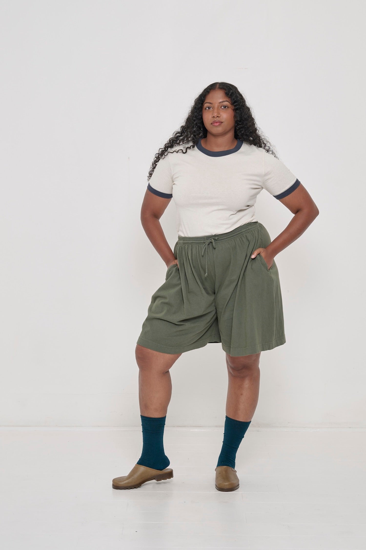 Front view of a woman in Pine Long Tubular Shorts with the Ringer Trash Tee in Slate tucked in. 