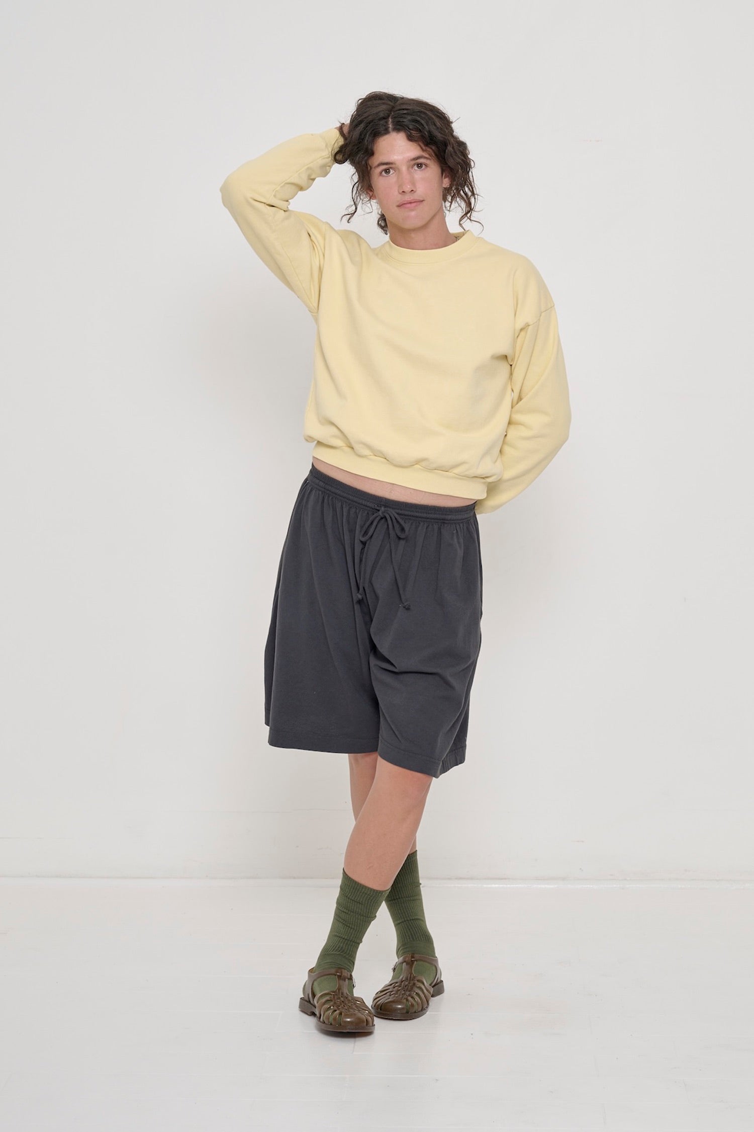 Slate Long Tubular Shorts, low-slung, with a French Butter Crewneck, hand behind head, exposing an inch of torso.