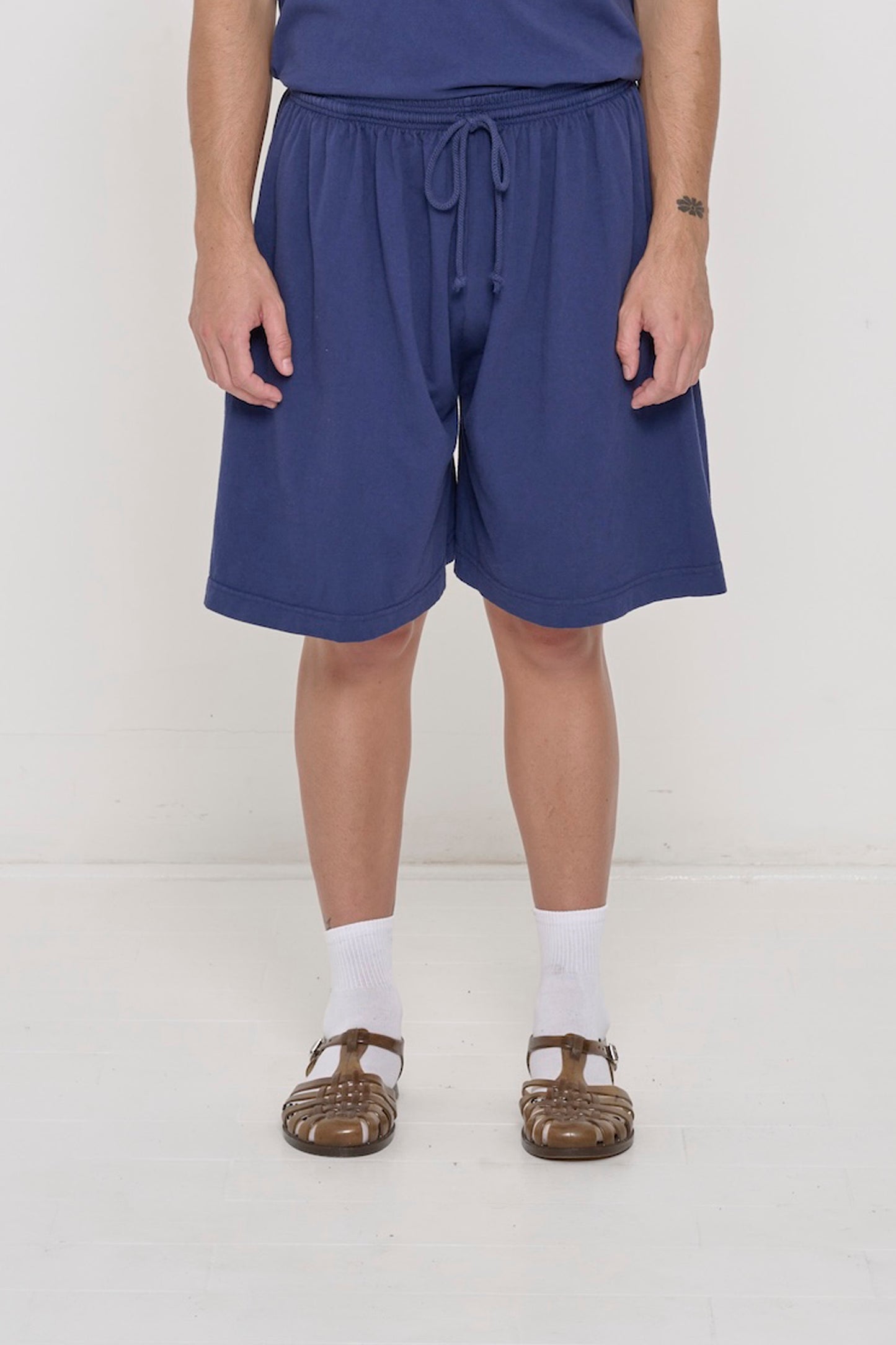 Front view person in Washed Navy Long Tubular Shorts, with waistband at the natural waist and  hem just above the knee.
