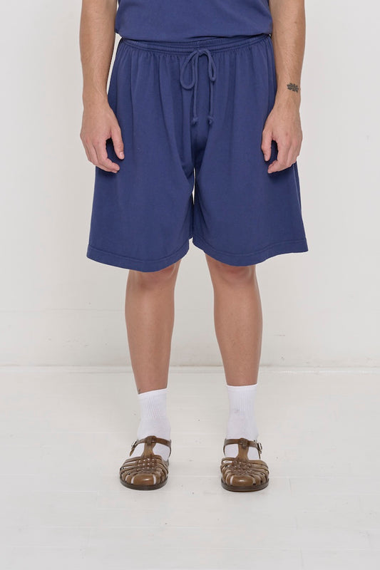 Front view person in Washed Navy Long Tubular Shorts, with waistband at the natural waist and  hem just above the knee.