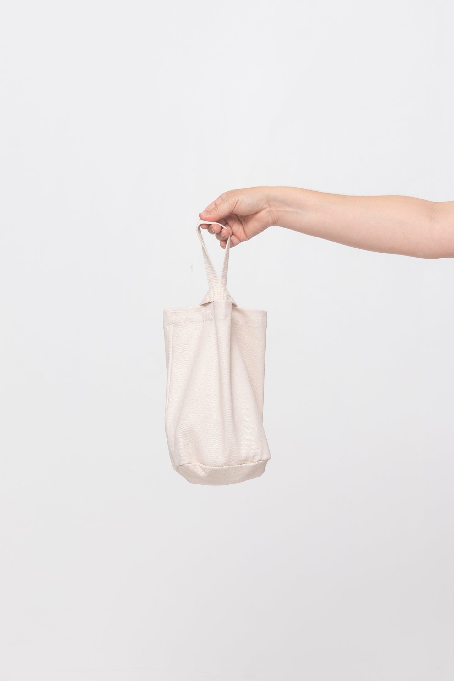 Natural Loop Tote, with longer strap facing the back, held in a person's hand, shows gussets, depth, stitching.