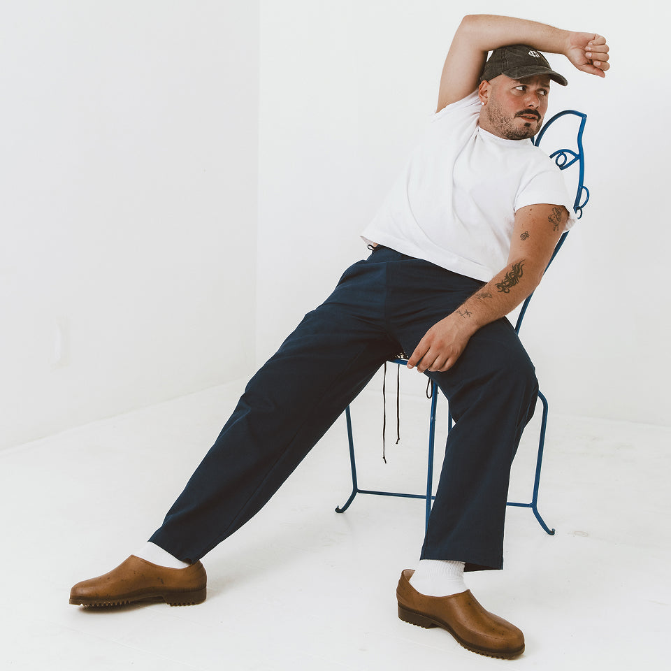 Man sitting in chair wearing Boxier Trash Tee in White and Cotton Twill Life Uniform Pants in Navy.