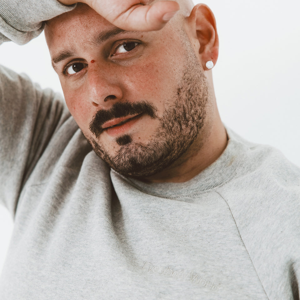 Close up of man resting is arm across his forehead, wearing a Heather Raglan Sweatshirt with a white background.