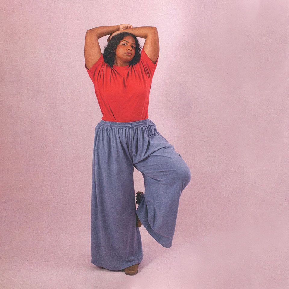 Woman wearing Periwinkle Tubular Pants and a Cedar Boxier Tee with her arms resting over her head.