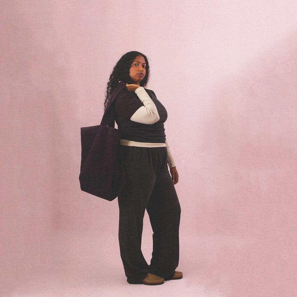 Woman with a Big Tote in Mulberry slung over thier shoulder against a pink background.