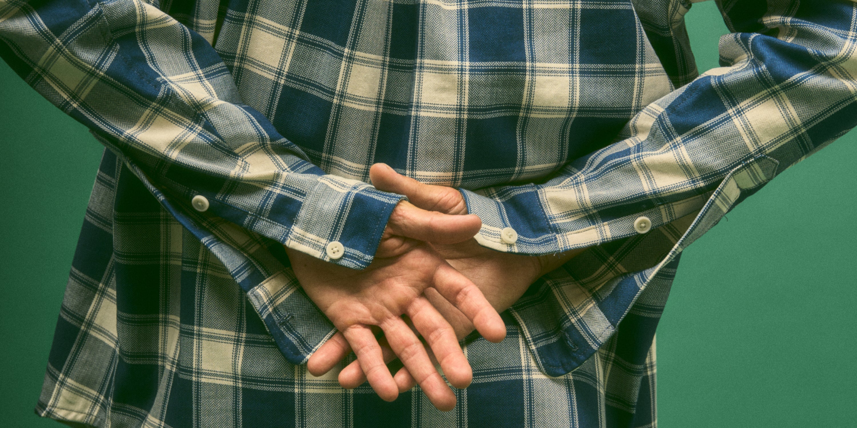 A model wearing a herringbone deadstock Plaid Button-Up Shirt with hands behind his back showing off the single button cuffs