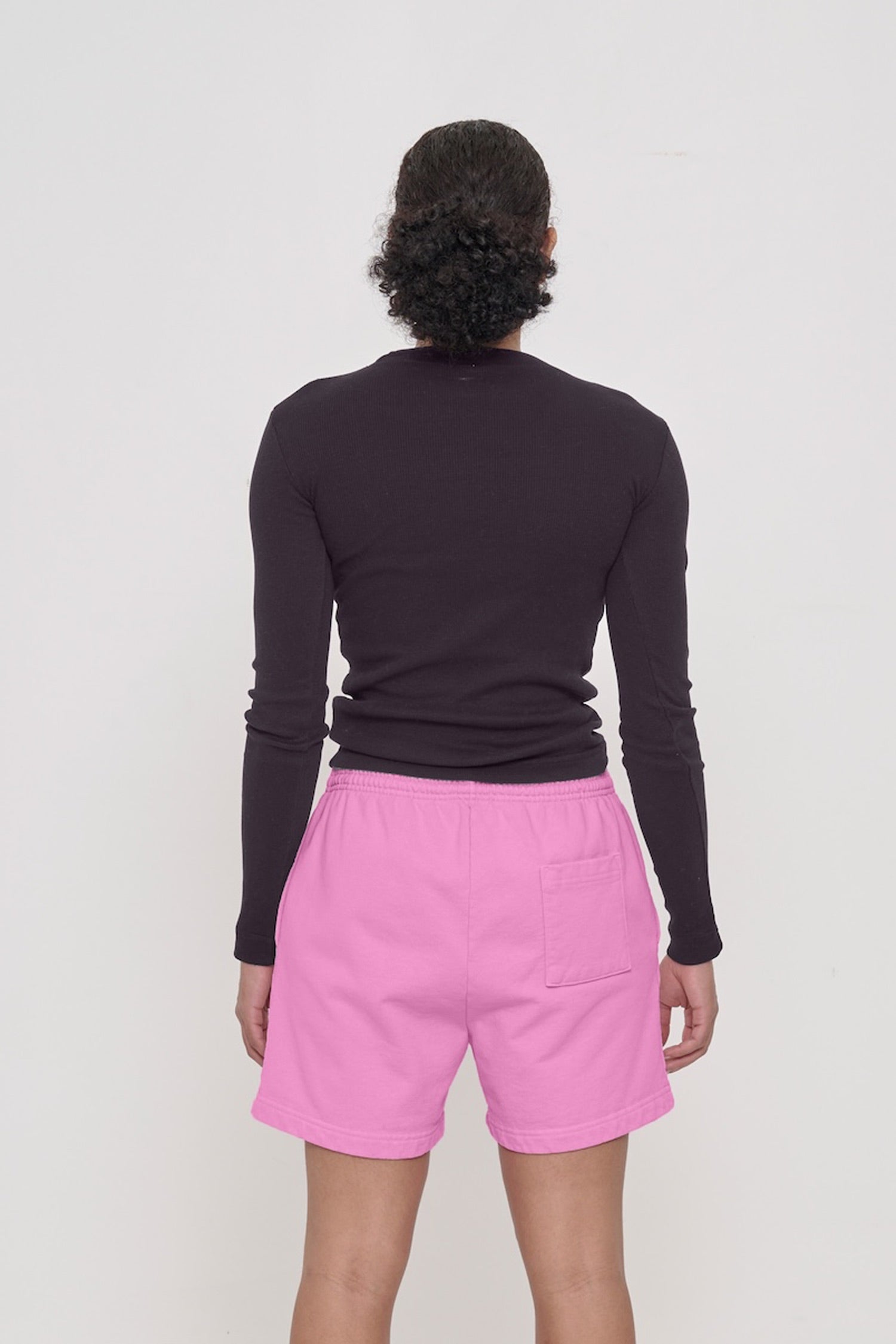 Back view: a woman in a Mulberry Rib Long Sleeve. Fitted across the upper back with a little bit of ease across her mid to lower back.